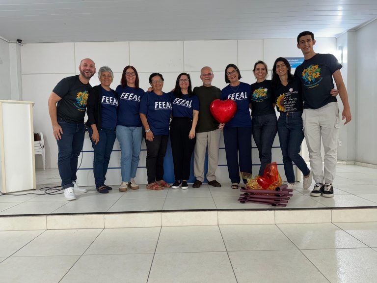 Grupo de colaboradores e dirigentes da FEEAL posando no auditório junto ao palestrante Gerardo Campana.