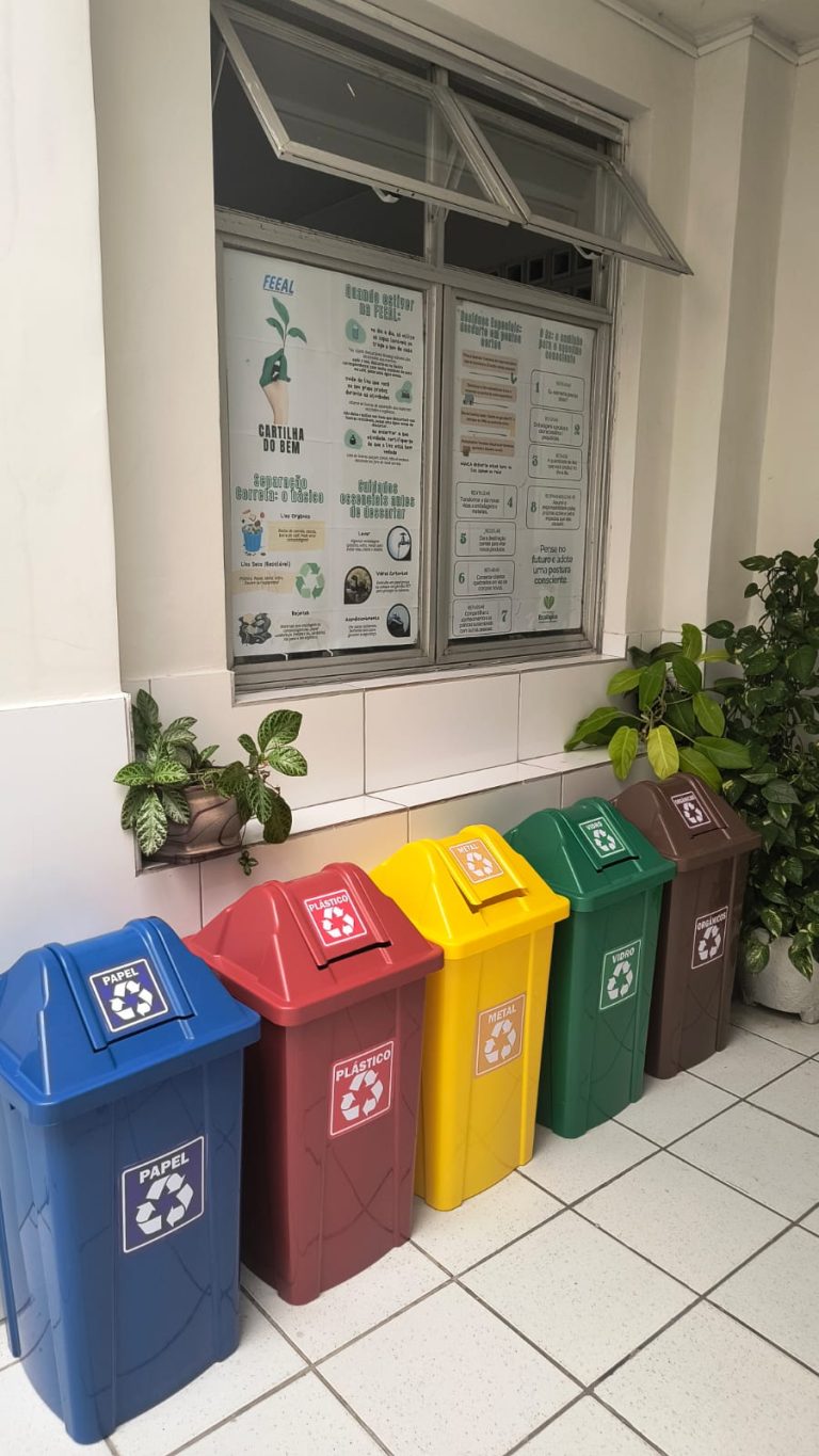 Lixeiras coloridas de coleta seletiva alinhadas no corredor ao lado da janela na FEEAL