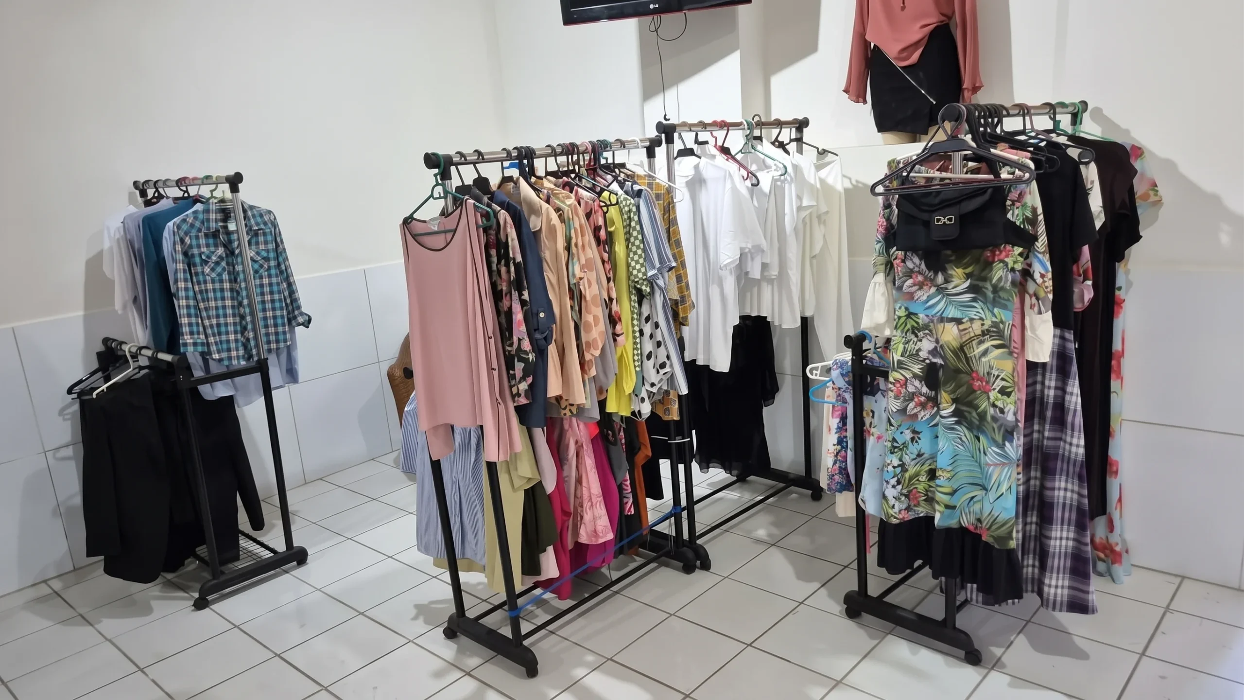 Araras com roupas e vestidos organizados em cabides no espaço do Bazar Fraterno da sede da FEEAL